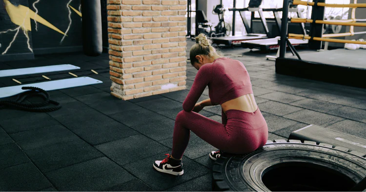 Person sitting on a gym tire looking exhausted after a workout, illustrating lack of motivation to exercise.